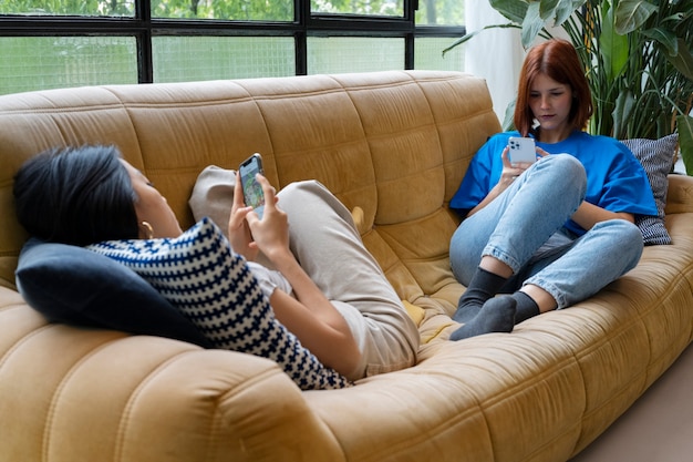 Mujeres de tiro completo acostadas en el sofá con teléfonos inteligentes