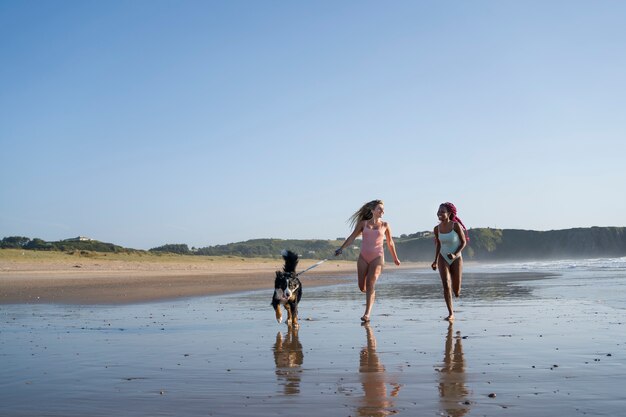 Mujeres de tiro completo corriendo en la playa con perro