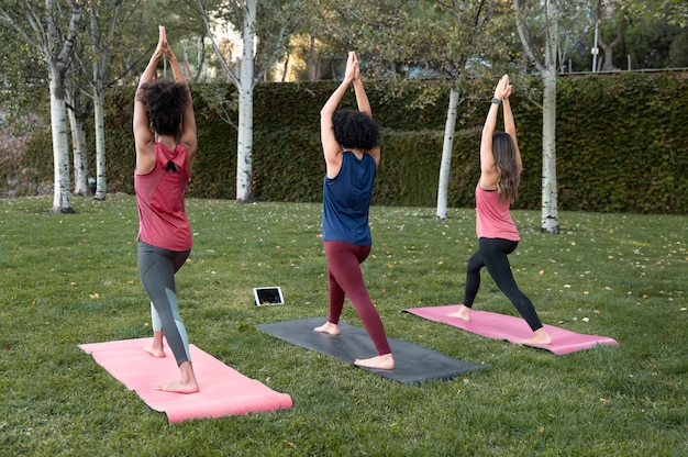 Mujeres de tiro completo haciendo yoga al aire libre