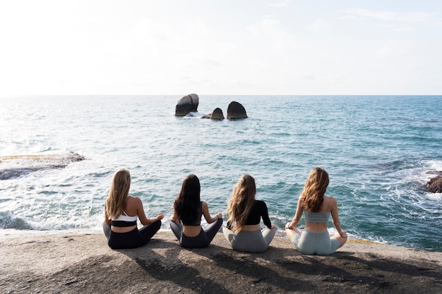 Mujeres de tiro completo meditando junto al mar.