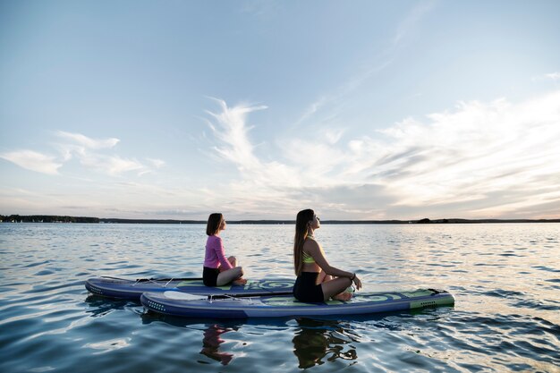 Mujeres de tiro completo meditando en paddleboard