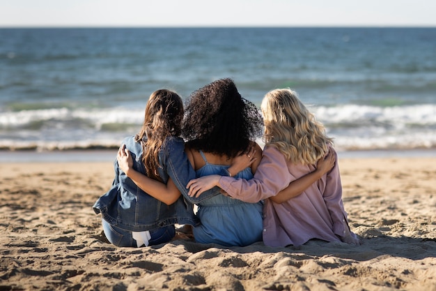 Mujeres de tiro completo sentadas juntas en la playa