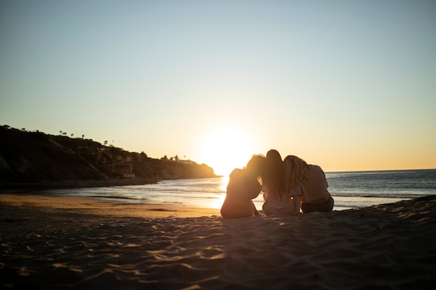 Mujeres de tiro completo sentadas en la playa al atardecer