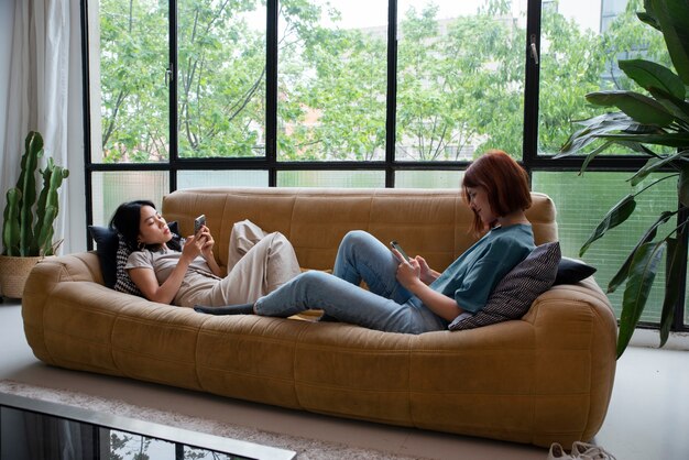 Mujeres de tiro completo sentadas en el sofá con teléfono inteligente