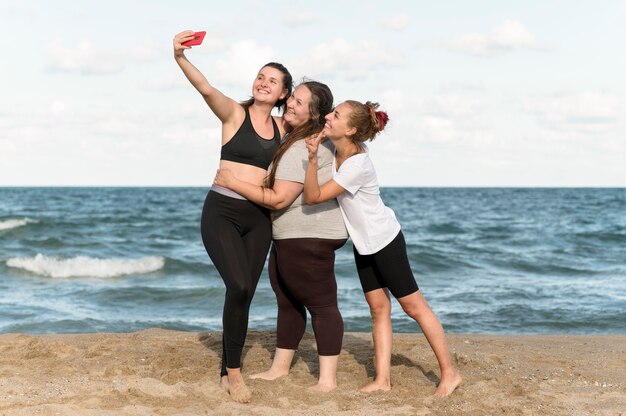 Mujeres de tiro completo tomando selfies en la playa