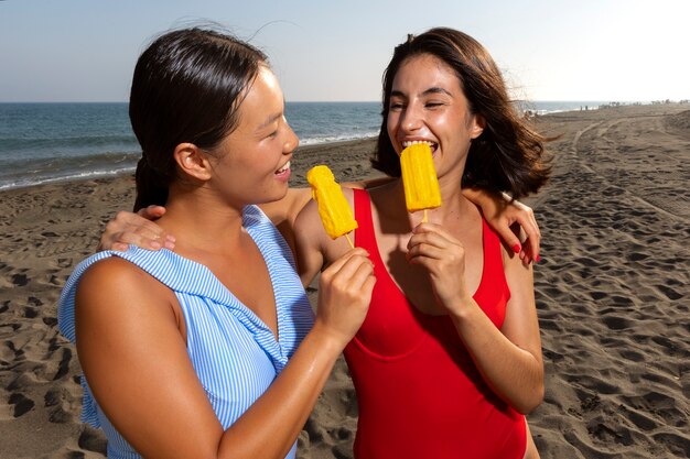 Mujeres de tiro medio comiendo helado en la playa