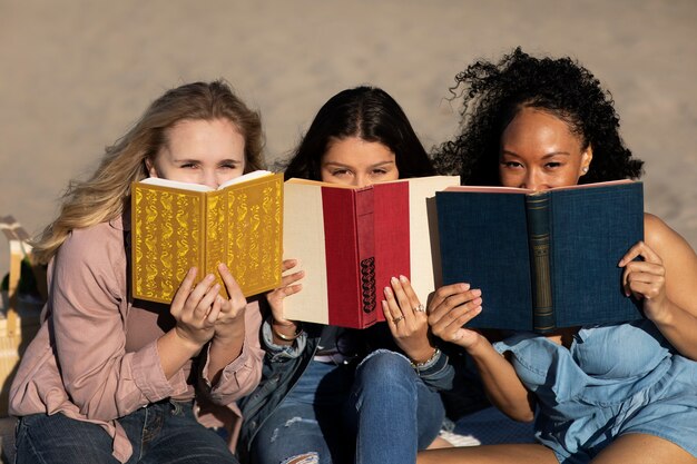 Mujeres de tiro medio sosteniendo libros en la playa