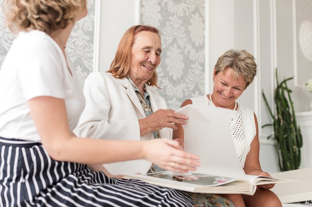 Mujeres de tres generaciones sentadas juntas y mirando el álbum de fotos en casa.