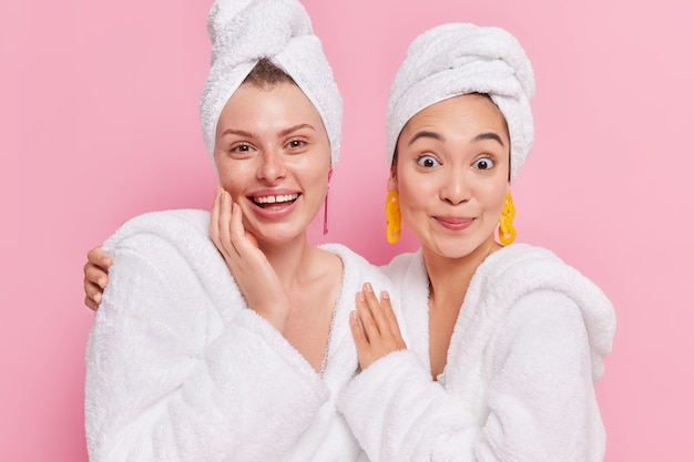 Las mujeres usan batas de baño blancas, toallas en la cabeza, pasan tiempo libre juntas después de los procedimientos de belleza y spa aislados en rosa