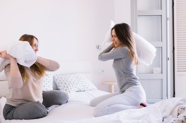 Foto gratuita mujeres de la vista lateral que tienen pelea de almohadas