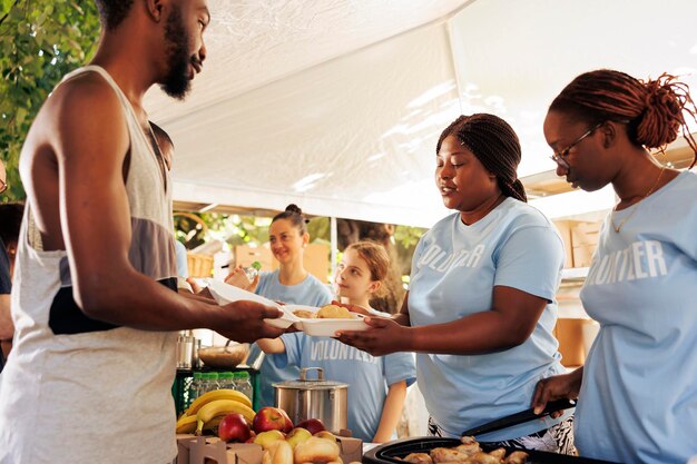 Mujeres voluntarias multiétnicas que sirven comida gratis al hombre sin hogar en un banco de alimentos al aire libre. El grupo sin fines de lucro ofrece ayuda humanitaria y fomenta la comunidad, ayudando a los hambrientos y menos privilegiados.