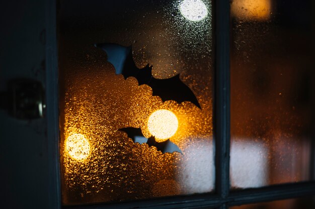 Murciélagos decorativos de Halloween pegados en la ventana con gotas de lluvia