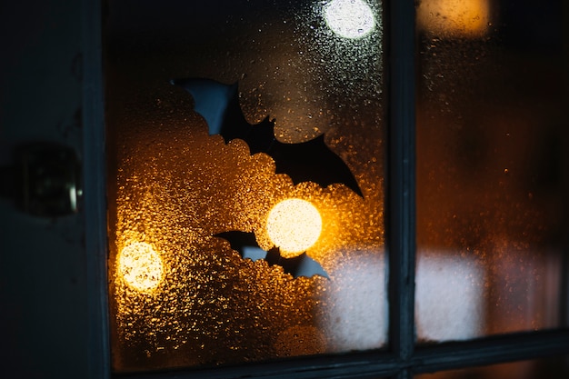 Murciélagos decorativos de Halloween pegados en la ventana con gotas de lluvia