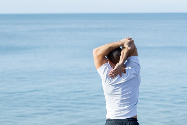 Muscular, deportivo, hombre, estirar, brazo, mar