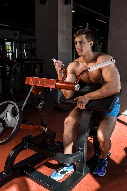 Los músculos tensos de las manos bajo carga. Hombre haciendo ejercicio para los bíceps en el gimnasio. Trabajar en los músculos de la palanca en el simulador. Fotos para revistas deportivas, carteles y sitios web.