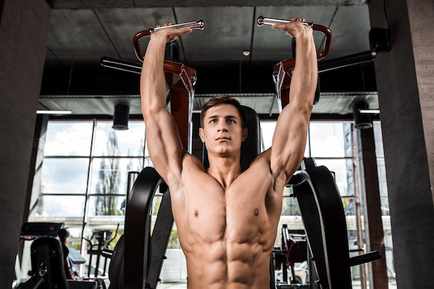 Foto gratuita los músculos tensos de las manos bajo carga. hombre haciendo ejercicio para los bíceps en el gimnasio. trabajar en los músculos de la palanca en el simulador. fotos para revistas deportivas, carteles y sitios web.