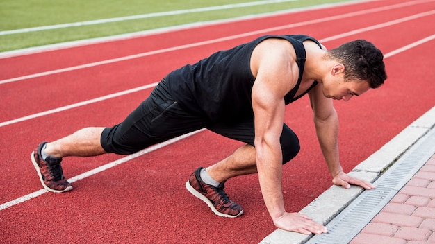 Un musculoso fitness joven haciendo flexiones en pista roja