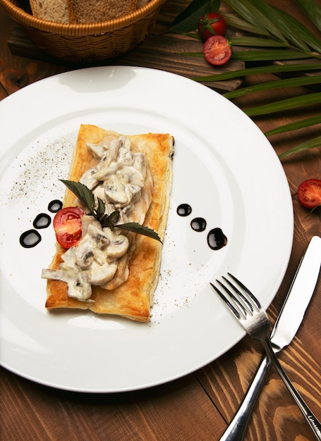 Mushtoom salteado, pollo stroganoff en un pedazo de pan. Antipasta en un plato blanco decorado con cubiertos en mesa de madera