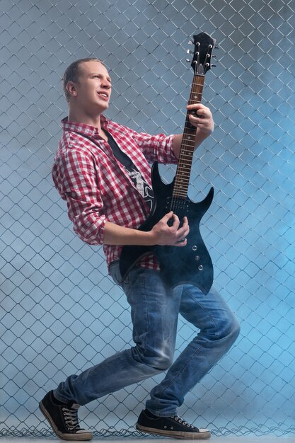 Música. Joven músico con una guitarra en la valla de la pared