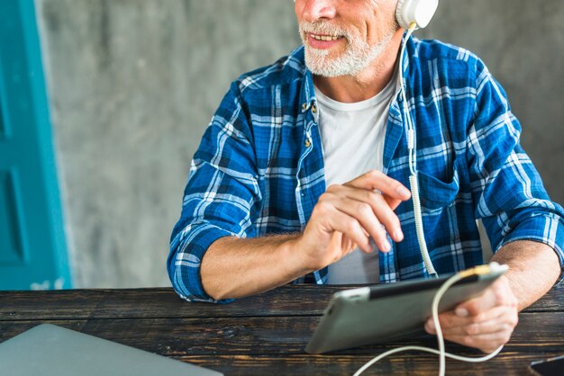 Música que escucha feliz del hombre mayor a través del auricular en la tableta digital