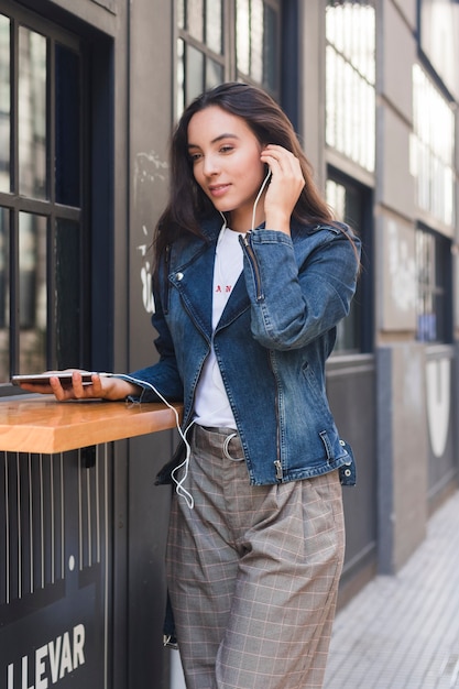 Música que escucha de moda de la mujer joven en el auricular a través del teléfono móvil