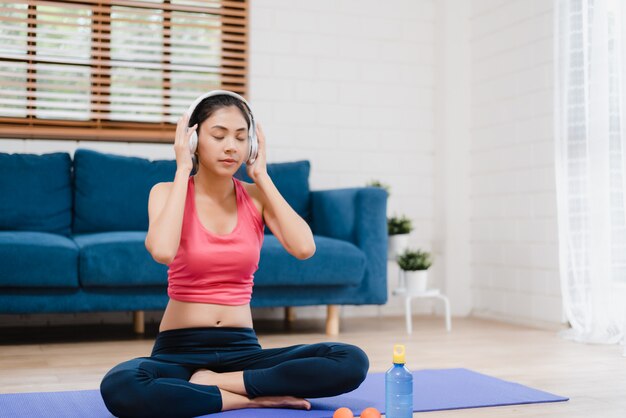 Música que escucha de la mujer asiática joven mientras que practica yoga en sala de estar