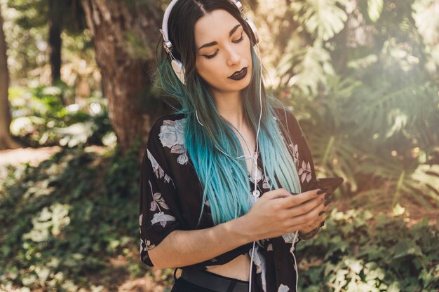 Música que escucha de la mujer en el auricular que hojea teléfono móvil