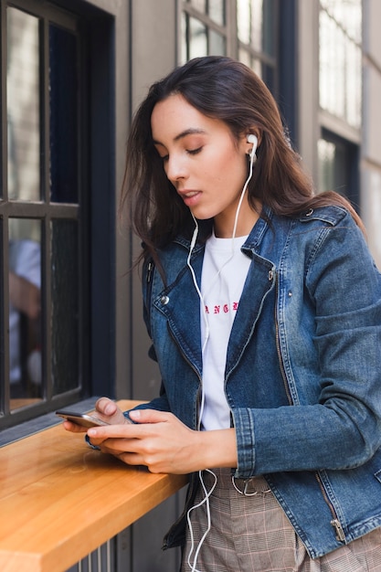 Música que escucha de la mujer joven en el auricular usando smartphone