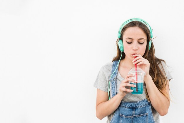 Música que escucha de la mujer joven en el jugo de consumición de los auriculares