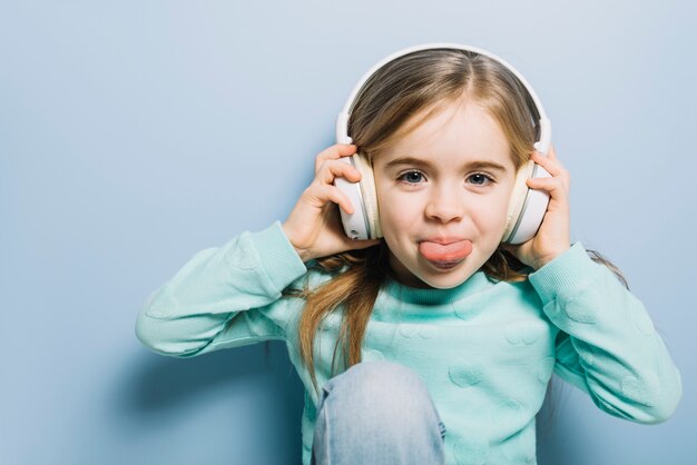 Música que escucha de la niña linda en el auricular que se pega la lengua hacia fuera