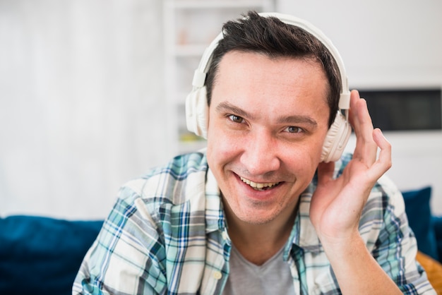 Música que escucha sonriente del hombre en auriculares en el sofá