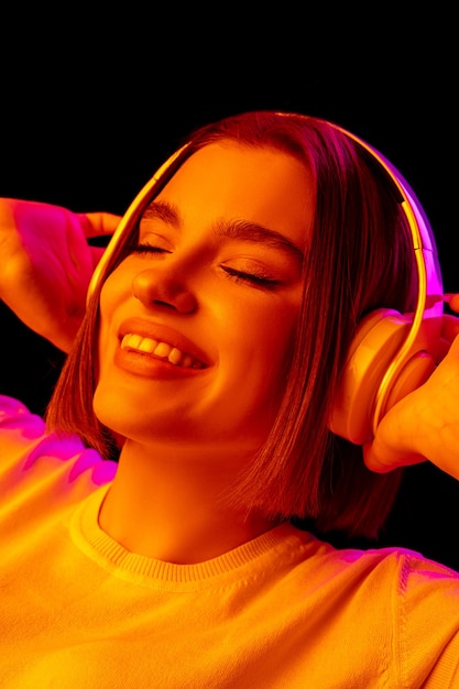 Música. Retrato de mujer caucásica sobre fondo de estudio rosa en luz de neón de moda. Hermosa modelo de mujer con auriculares. Concepto de emociones humanas, expresión facial, ventas, publicidad, moda.