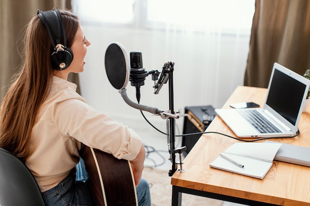 Músico femenino en casa grabando canciones y tocando la guitarra acústica