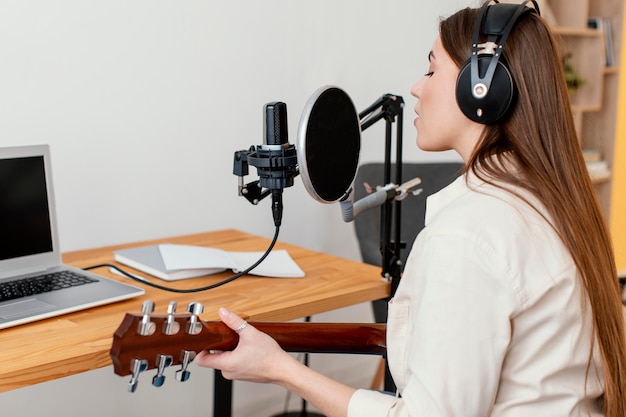 Músico femenino grabando la canción mientras toca la guitarra acústica en casa