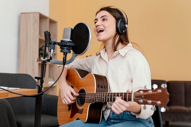 Músico femenino grabando canciones y tocando la guitarra acústica en casa