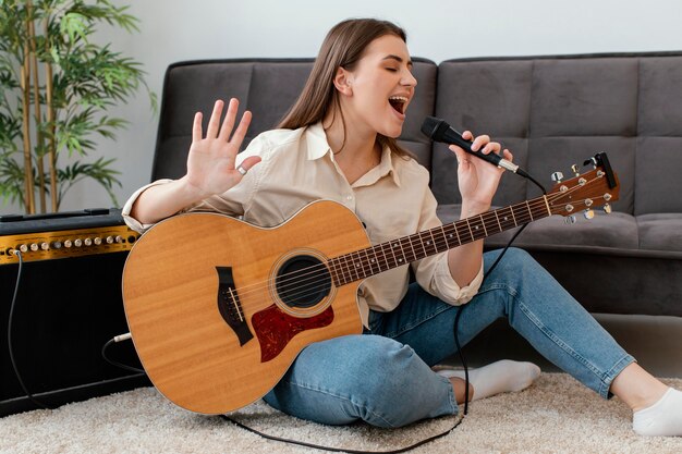 Músico femenino sonriente tocando la guitarra acústica y cantando en el micrófono