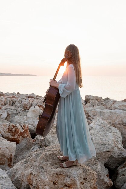 Músico femenino con violonchelo en rocas