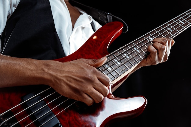 Foto gratuita músico de jazz guapo afroamericano tocando el bajo en el estudio sobre un fondo negro. concepto de música. chico atractivo alegre joven improvisando. retrato retro de primer plano.