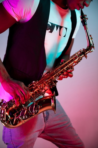 Foto gratuita músico de jazz guapo afroamericano tocando el saxofón en el estudio sobre un fondo de neón. concepto de música. chico atractivo alegre joven improvisando. retrato retro de primer plano.
