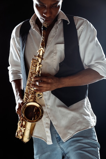 Músico de jazz tocando el saxofón en el estudio sobre una pared negra