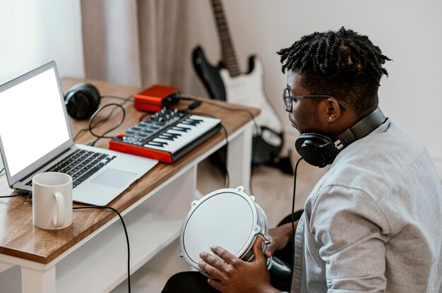 Músico masculino en casa tocando la batería y mezclando con un portátil