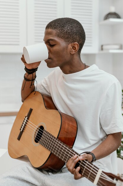 Músico masculino en casa tocando la guitarra y bebiendo de taza