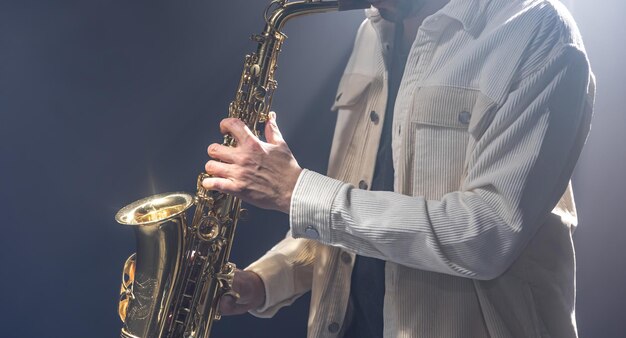 Músico masculino en el escenario toca el saxofón oscuro con humo