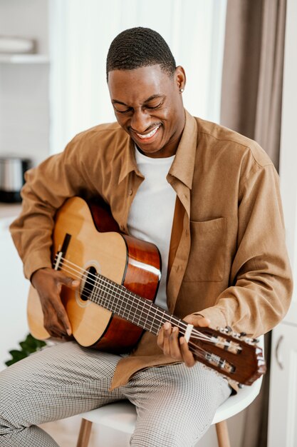 Músico masculino sonriente en casa tocando la guitarra