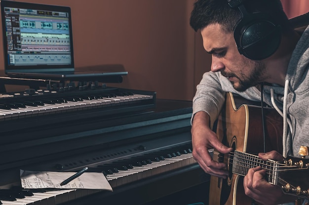 Músico masculino toca la guitarra en casa en el lugar de trabajo cerca de la computadora