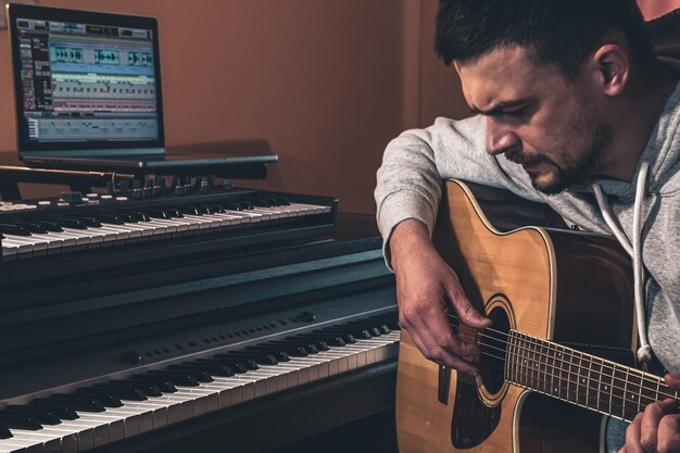 Músico masculino toca la guitarra en casa en el lugar de trabajo cerca de la computadora