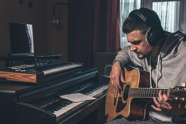 Músico masculino toca la guitarra en casa en el lugar de trabajo cerca de la computadora