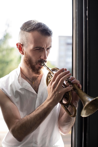 Músico masculino tocando la corneta junto a la ventana