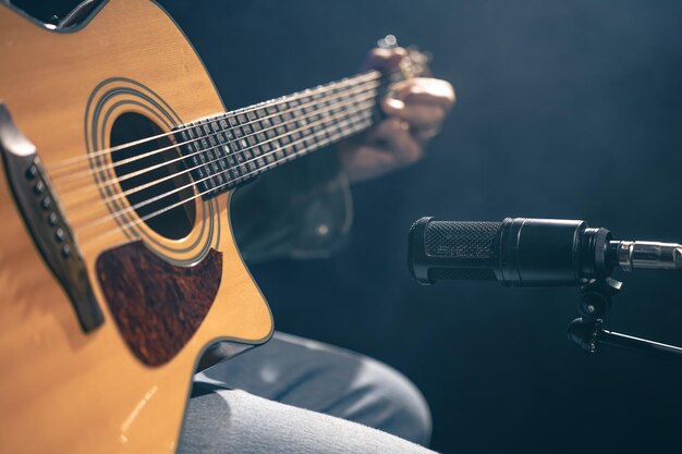 Músico masculino tocando la guitarra acústica detrás del micrófono en un estudio de grabación