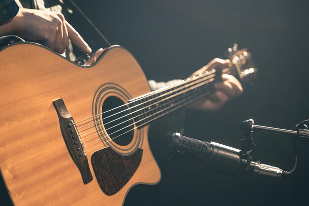 Foto gratuita músico masculino tocando la guitarra acústica detrás del micrófono en un estudio de grabación